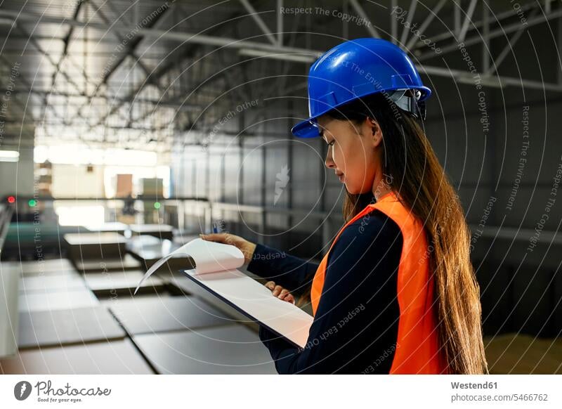 Female worker checking documents in factory warehouse scrutiny scrutinizing woman females women paper papers female workers magazine factories Adults grown-ups