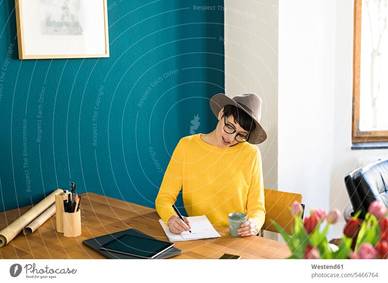Businesswoman in home office writing on a piece of paper holding coffee mug at home females women write working At Work apartment flats apartments businesswoman