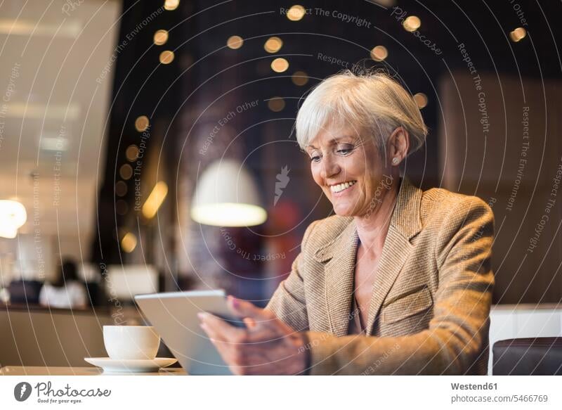 Smiling senior businesswoman using tablet in a cafe businesswomen business woman business women females digitizer Tablet Computer Tablet PC Tablet Computers