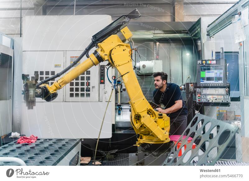 Young male worker analyzing robotic arm in manufacturing factory color image colour image indoors indoor shot indoor shots interior interior view Interiors