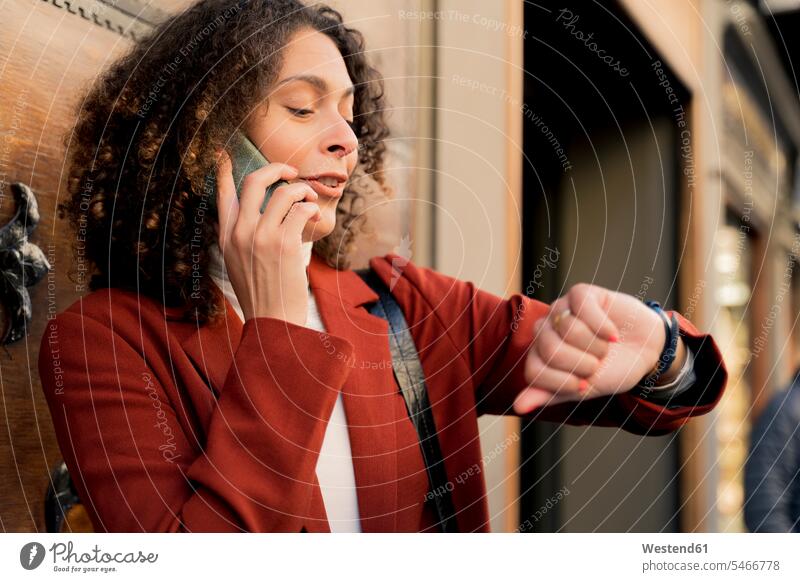 Woman on the phone in the city checking the time human human being human beings humans person persons curl curled curls curly hair coat coats jackets watches