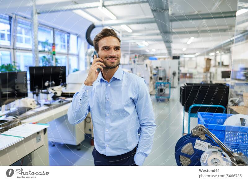 Smiling young male professional talking on smart phone while standing at illuminated factory color image colour image indoors indoor shot indoor shots interior