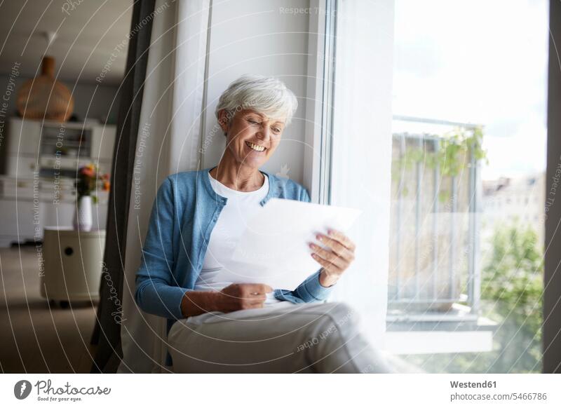 Senior woman reading letter happily while sitting on window at home color image colour image indoors indoor shot indoor shots interior interior view Interiors