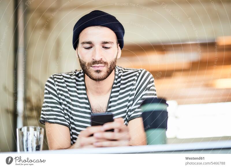 Young man wearing a beanie using cell phone beanies stocking cap stocking caps stocking-cap mobile phone mobiles mobile phones Cellphone cell phones hats