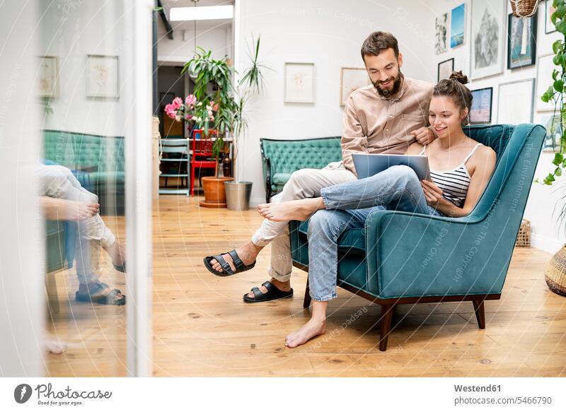 Young couple sitting in arm chair, using digital tablet human human being human beings humans person persons caucasian appearance caucasian ethnicity european 2