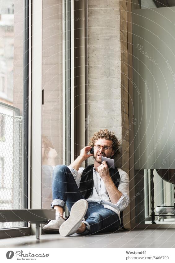 Casual young man sitting at the window with headphones and phablet men males mobile phone mobiles mobile phones Cellphone cell phone cell phones headset windows