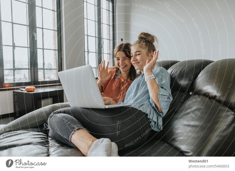 Friends waving while video conferencing over laptop on sofa at home color image colour image Germany indoors indoor shot indoor shots interior interior view