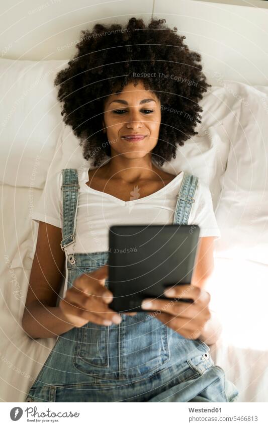 Smiling woman lying in bed reading e-book beds females women laying down lie lying down E-Book ebook electronic book smiling smile Adults grown-ups grownups