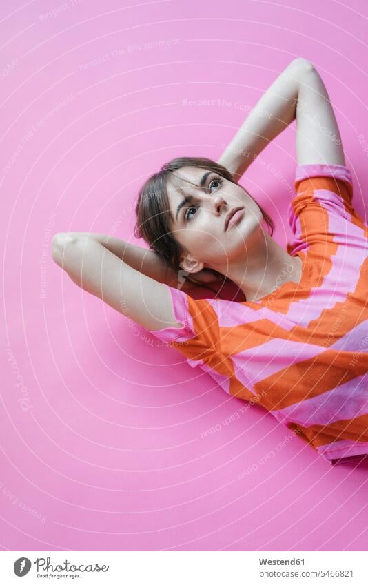 Woman lying on pink background with hands behind head, thinking magenta laying down lie lying down hands behind neck Hand Behind Head daydreaming day dreaming