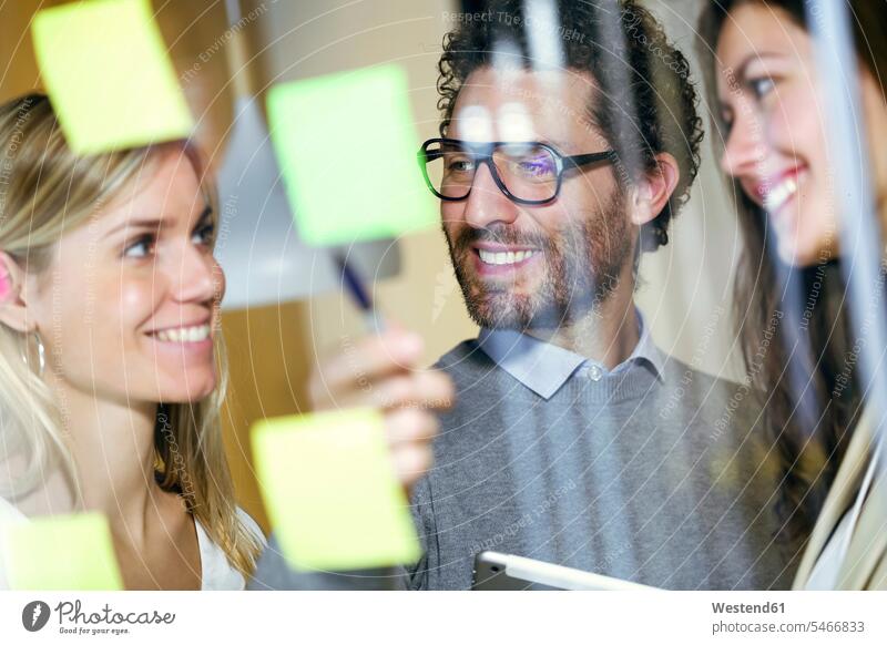 Three smiling business people brainstorming together with sticky notes on a glass wall human human being human beings humans person persons caucasian appearance