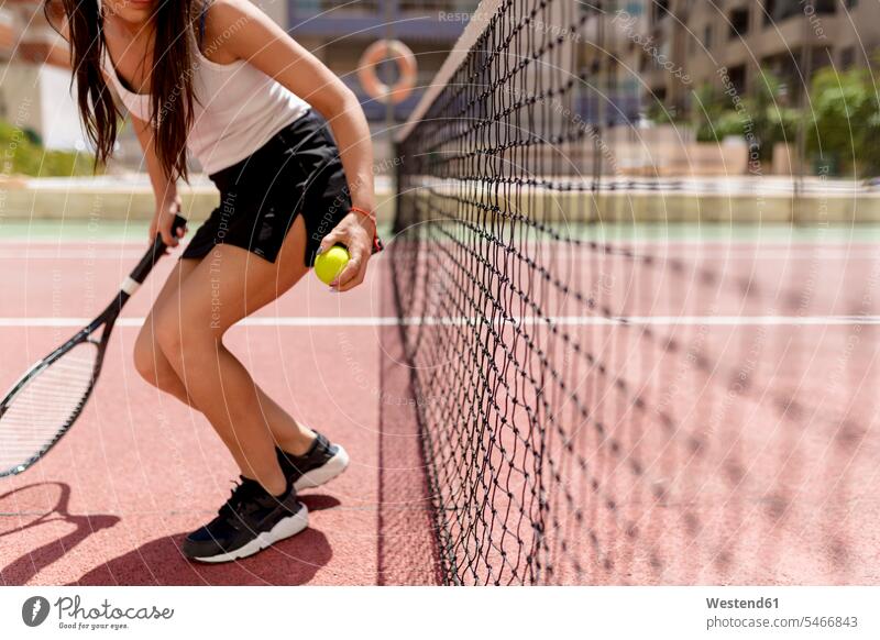 Female tennis player holding racket and ball while standing by net in court color image colour image Spain outdoors location shots outdoor shot outdoor shots