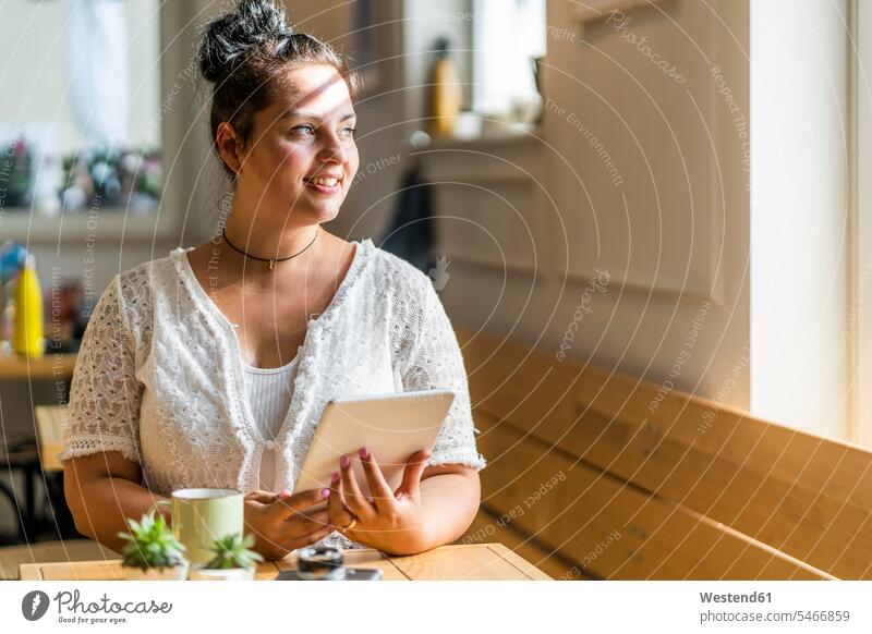 Thoughtful young woman with digital tablet sitting at table in coffee shop color image colour image indoors indoor shot indoor shots interior interior view