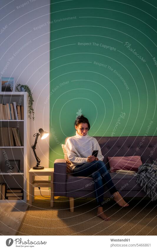 Woman using smart phone while sitting on sofa at home color image colour image indoors indoor shot indoor shots interior interior view Interiors day
