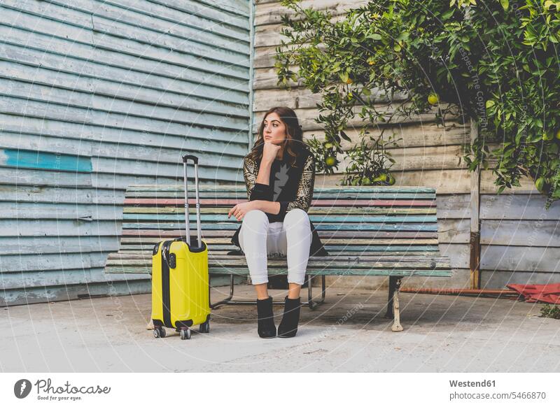 Young woman with yellow trolley bag waiting on a bench benches females women Trolley Bag Adults grown-ups grownups adult people persons human being humans