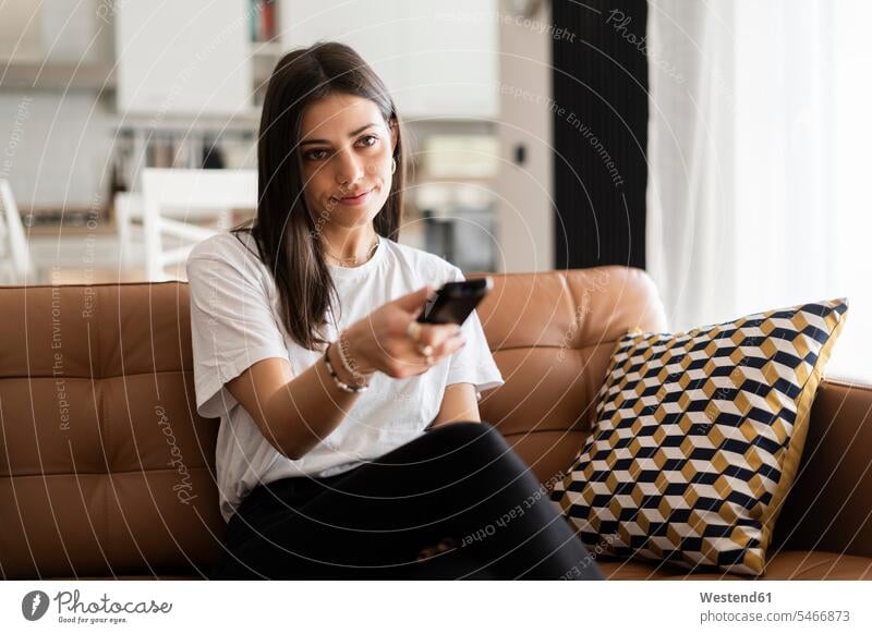 Young woman sitting on couch at home watching Tv human human being human beings humans person persons celibate celibates singles solitary people solitary person