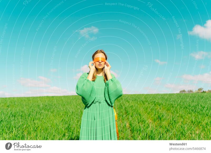 Blindfolded young woman wearing a green dress standing in a field band bands ribbons dresses touch relax relaxing feel seasons spring season Spring Time