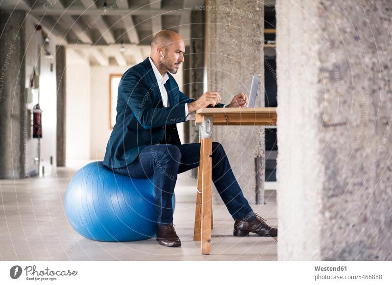 Man using laptop while sitting on fitness ball at office color image colour image indoors indoor shot indoor shots interior interior view Interiors day