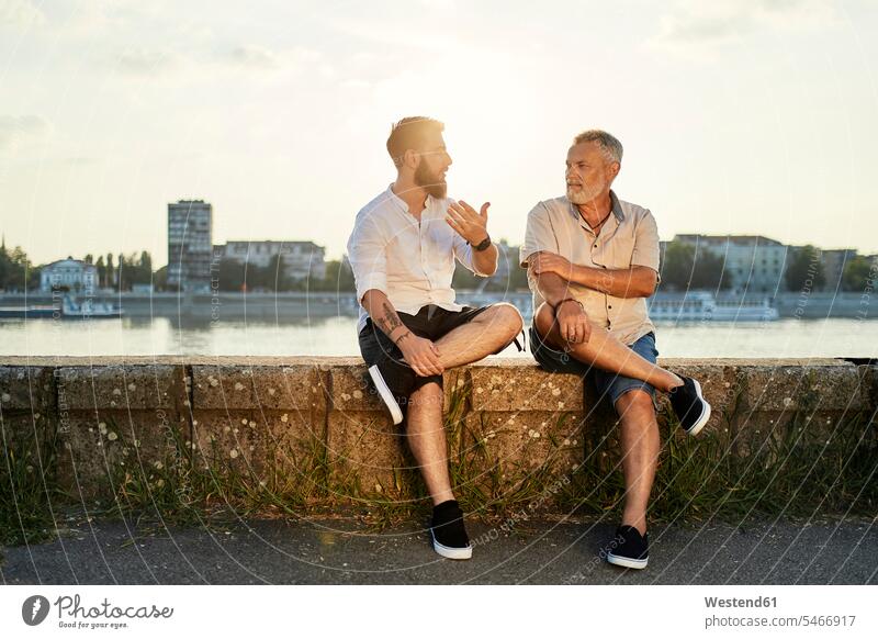 Father and adult son sitting on a wall at the riverside talking human human being human beings humans person persons caucasian appearance caucasian ethnicity