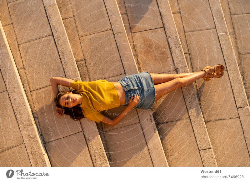 Young woman lying on steps outdoors females women laying down lie lying down stair Adults grown-ups grownups adult people persons human being humans
