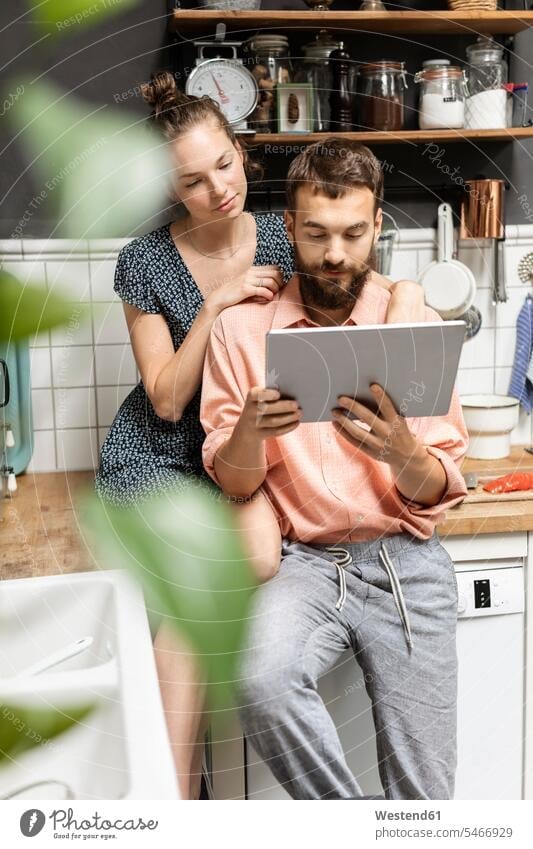 Young couple using digital tablet in kitchen recipes rack racks Shelve shelves closeness propinquity at home Distinct individual Technological technologies