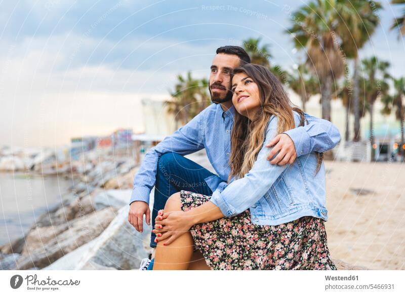 Spain, Barcelona, couple sitting on rocks at the seaside twosomes partnership couples together coast coastline coast area Seacoast Seated people persons