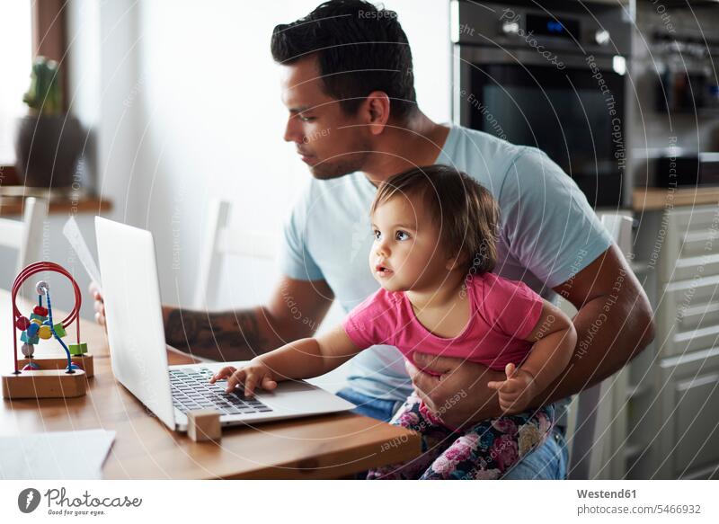 Father with baby girl using laptop on table at home daughter daughters Table Tables father pa fathers daddy dads papa Laptop Computers laptops notebook infants