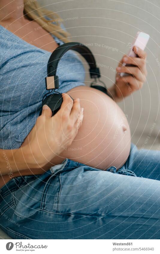 Mid-section of pregnant woman holding headphones at her belly bellies abdomen human abdomen females women headset Pregnant Woman people persons human being
