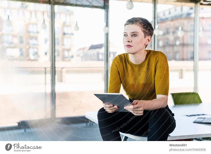 Thoughtful businesswoman sitting on desk in office holding tablet human human being human beings humans person persons caucasian appearance caucasian ethnicity
