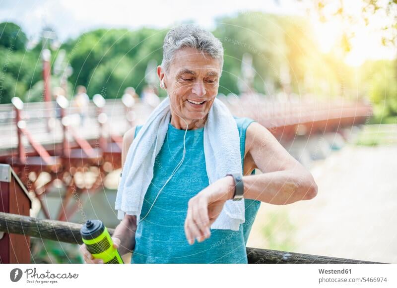 Smiling active senior man looking at smart watch while standing in park color image colour image outdoors location shots outdoor shot outdoor shots day
