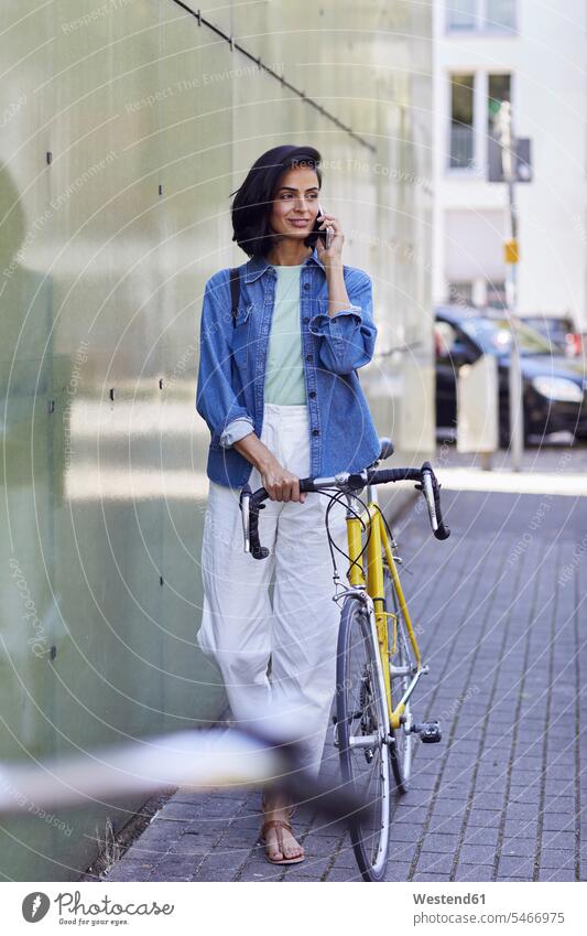 Female commuter talking over smart phone while standing with bicycle on street in city color image colour image Germany businesswoman businesswomen