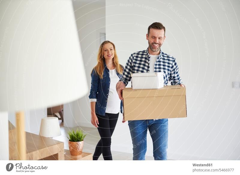 Happy couple moving into new flat carrying cardboard box cardboard boxes packing case packing cases move in happiness happy twosomes partnership couples flats