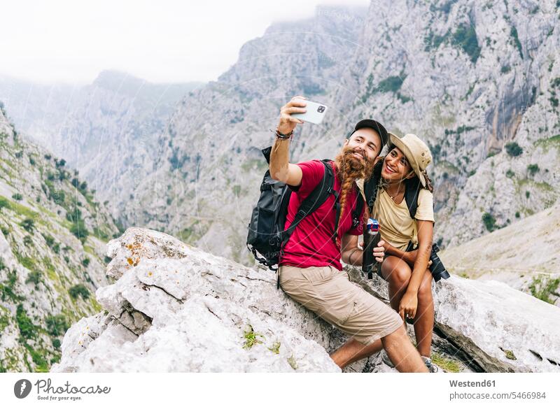 Smiling couple taking selfie while sitting on rock at Ruta Del Cares, Asturias, Spain color image colour image outdoors location shots outdoor shot