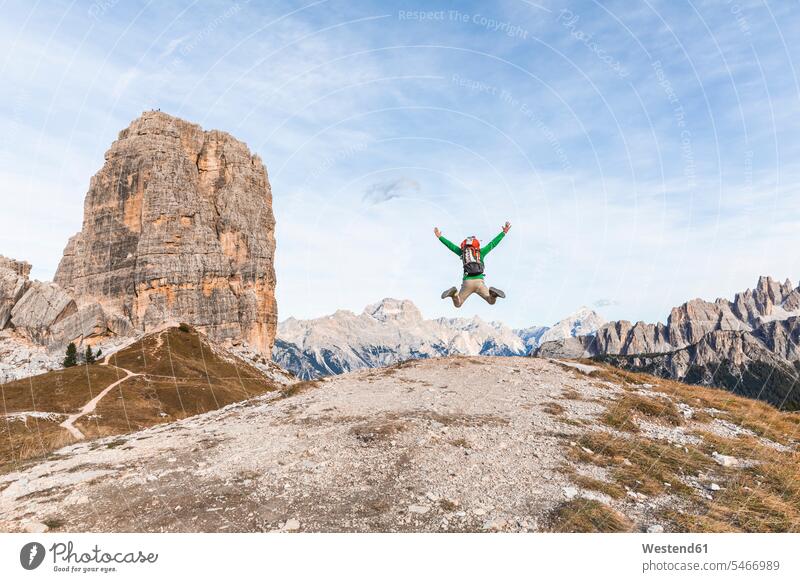 Italy, Cortina d'Ampezzo, happy hiker jumping at the top of the mountain in the Dolomites mountains hiking wanderers hikers man men males happiness summit