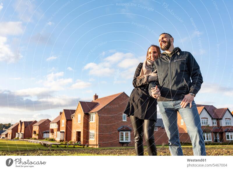 Happy couple looking away while standing outside newly built houses against sky color image colour image day daylight shot daylight shots day shots daytime