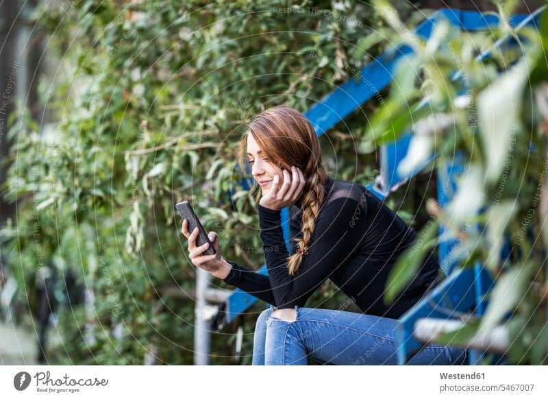 Smiling woman sitting on stairs looking at smartphone Smartphone iPhone Smartphones stairway Seated females women eyeing mobile phone mobiles mobile phones