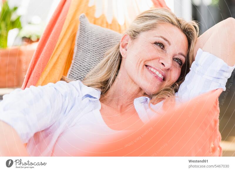 Portrait of happy mature woman relaxing in hammock cushions hammocks smile delight enjoyment Pleasant pleasure laying down lie lying down at home free time