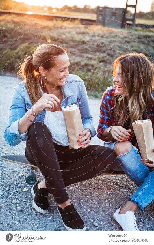 Two laughing friends sitting on longboard eating popcorn female friends Popcorn Popcorns Laughter Longboard Seated mate friendship Sweets Candies Sweet Food