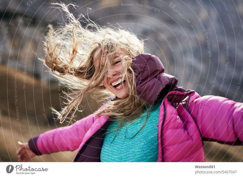 Happy young woman leaning against the wind in the mountains laughing Laughter females women portrait portraits Windswept Windblown Windy hiker wanderers hikers