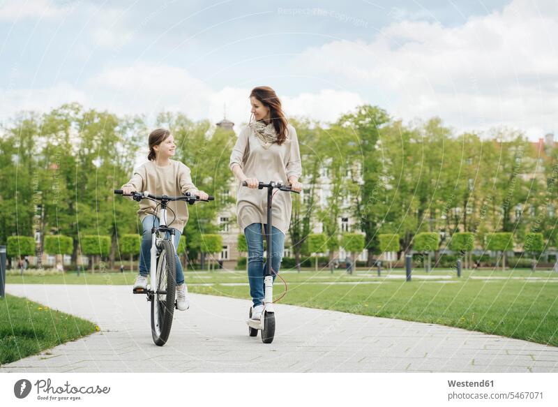Girl cycling while mother riding electric scooter in city park color image colour image leisure activity leisure activities free time leisure time