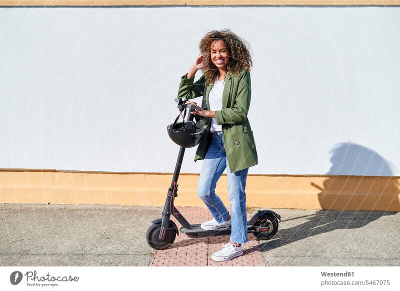 Happy woman standing with electric push scooter on sidewalk during sunny day color image colour image outdoors location shots outdoor shot outdoor shots