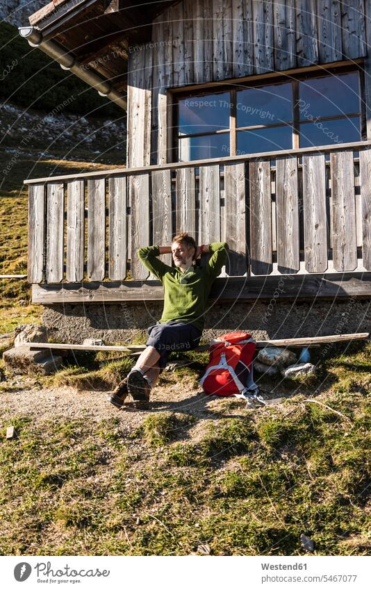 Mature man relaxing at a mountain hut, enjoying the sun backpack rucksacks backpacks back-packs mountain shelter alpine hut mountain huts mountain lodge