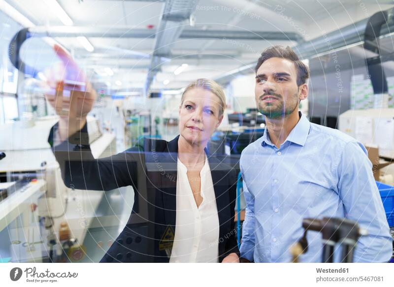 Confident businesswoman planning with young engineer while pointing at glass interface in factory color image colour image indoors indoor shot indoor shots