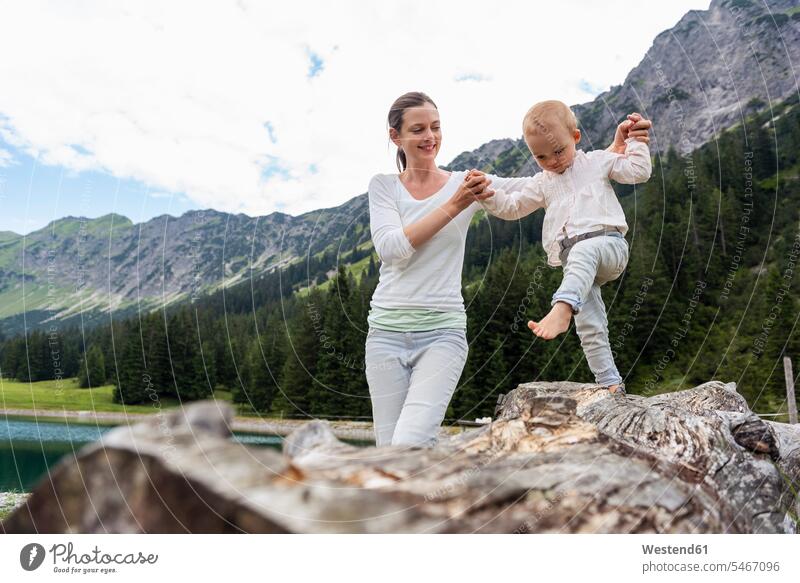 Germany, Bavaria, Oberstdorf, mother helping little daughter balancing on a log mommy mothers mummy mama balance assistance assisting Help daughters parents
