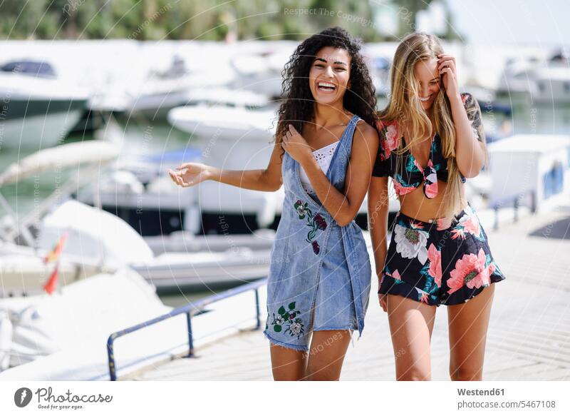 Two laughing young women at waterfront promenade in summer summer time summery summertime female friends promenades Laughter woman females mate friendship