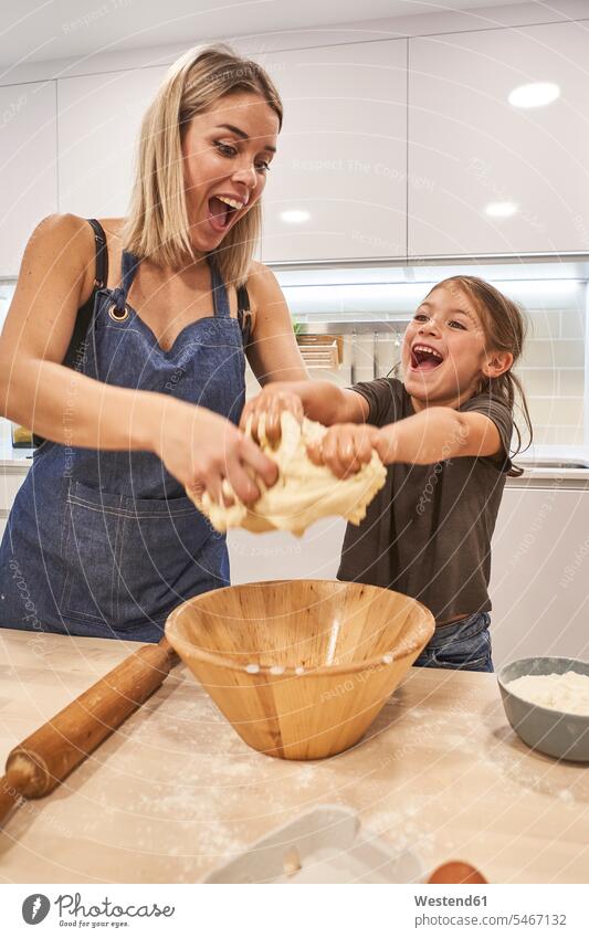 Playful mother and daughter screaming while kneading pizza dough in kitchen at home color image colour image Spain leisure activity leisure activities free time