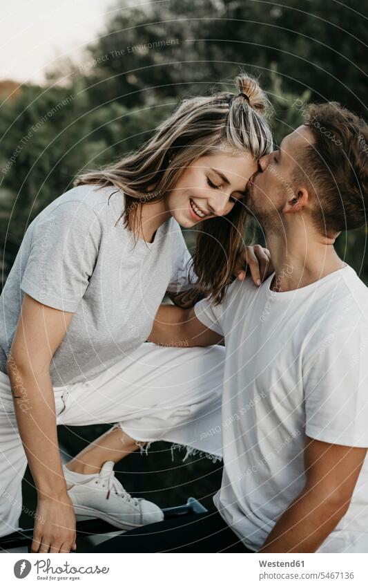 Portrait of young smiling couple, man kissing her on the forehead T- Shirt t-shirts tee-shirt embrace Embracement hug hugging in the evening delight enjoyment