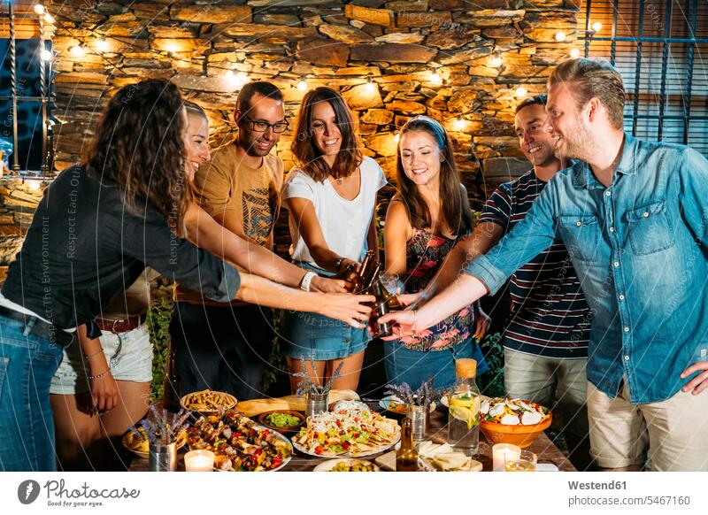 Happy friends toasting with beer bottles during an outdoor dinner mate Bottles Beer Bottles dish dishes Plates Tables relax relaxing celebrate partying hold