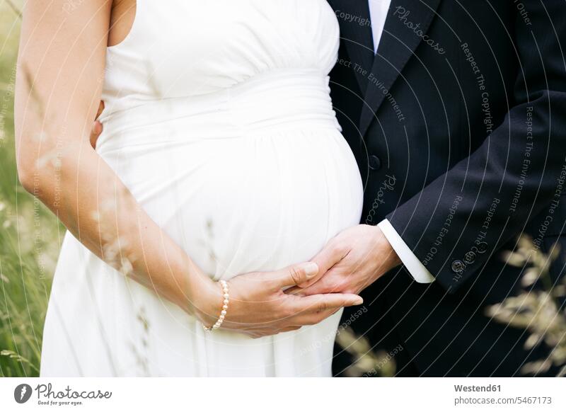 Pregnant bride with her husband holding baby belly on a meadow human human being human beings humans person persons marriage matrimony couple married couples