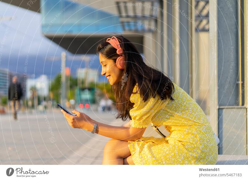 Happy woman using smart phone and listening music while sitting in city color image colour image outdoors location shots outdoor shot outdoor shots day