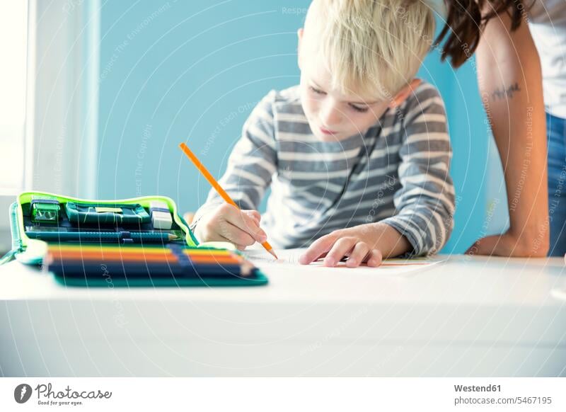 Boy doing homework with mother leaning on desk Home work boy boys males mommy mothers mummy mama desks child children kid kids people persons human being humans